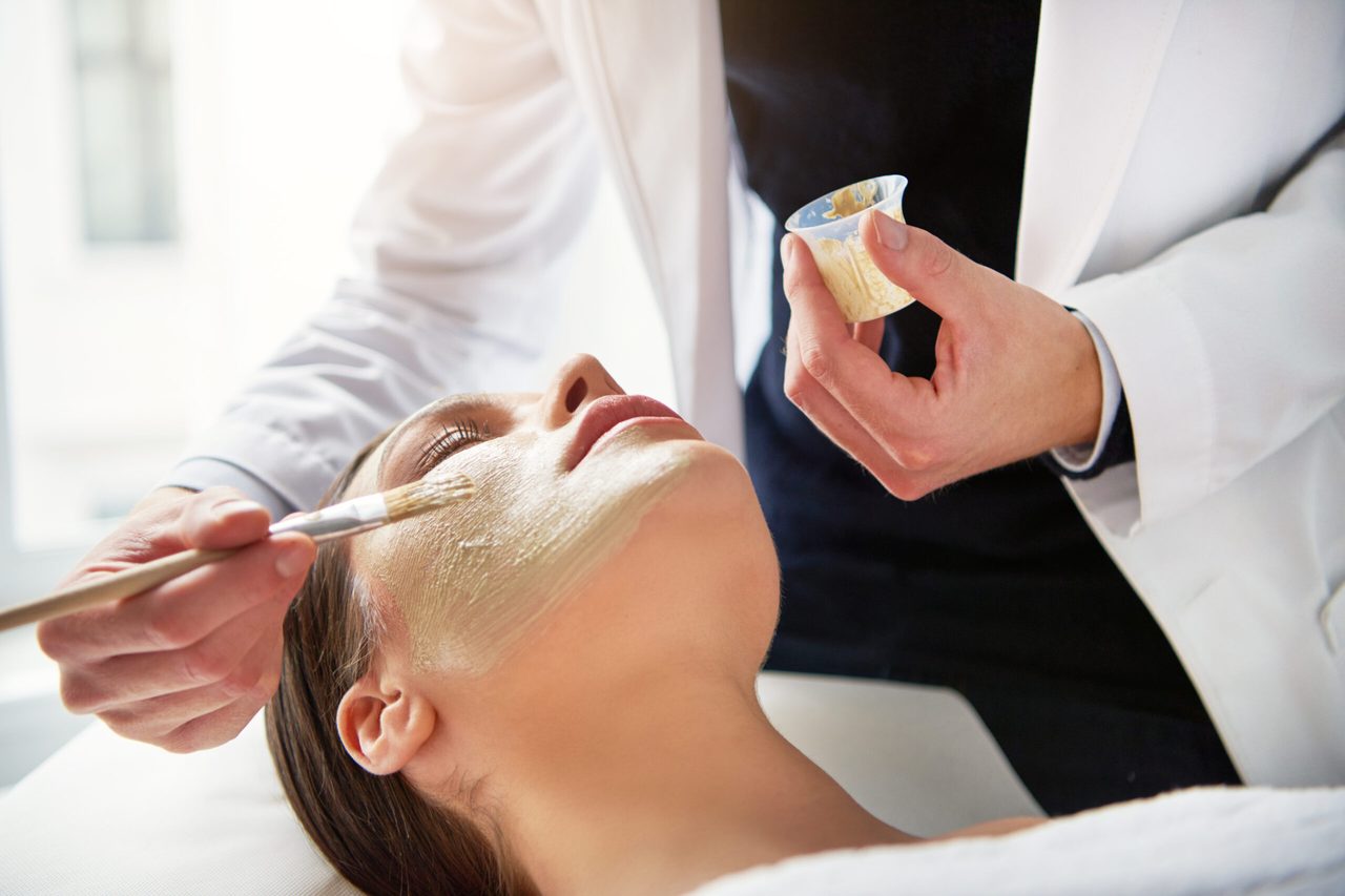 A therapist applying a mask with a brush during a facial treatment.
