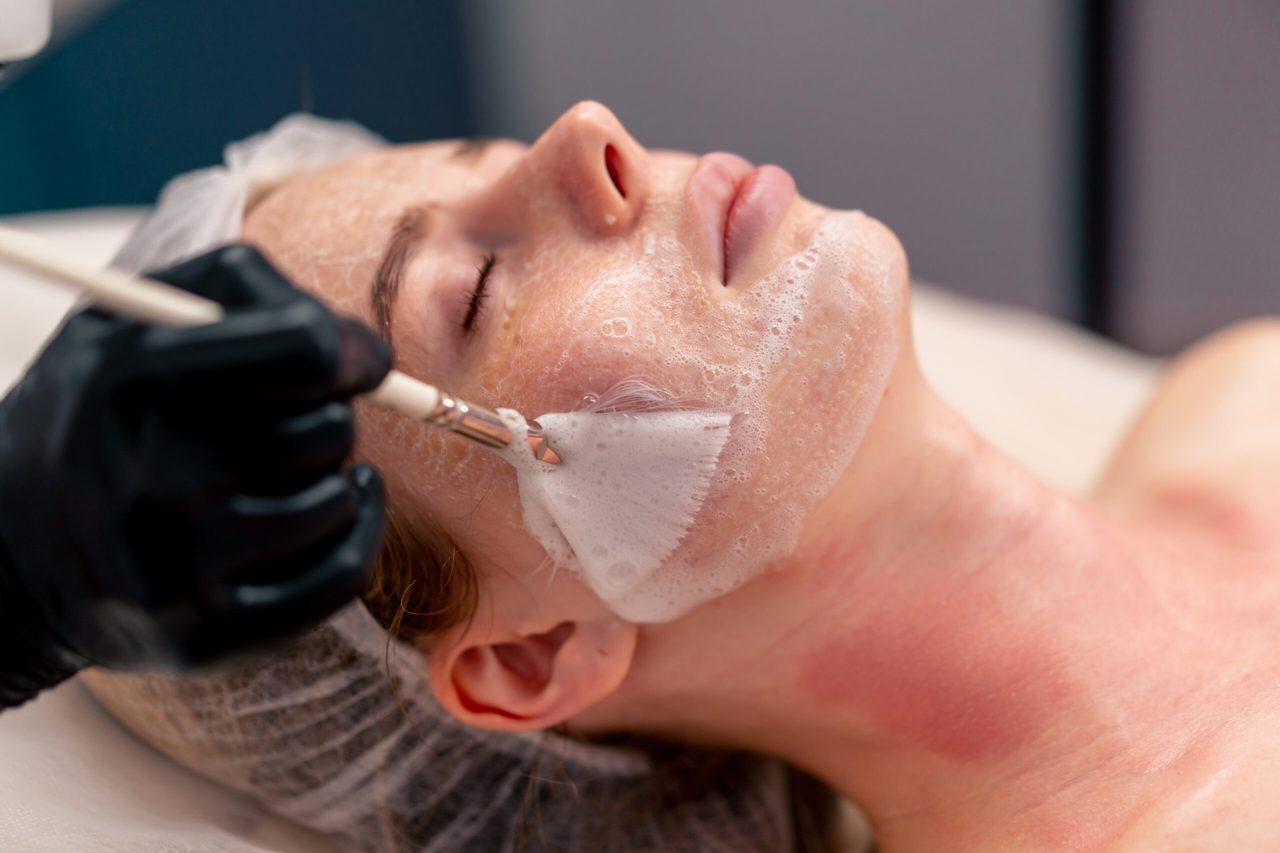 A cleansing foam being brushed across the cheek during a facial.