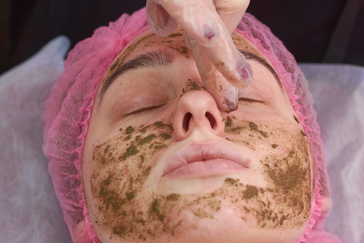 A green herbal mask being worked into the skin during a peel.