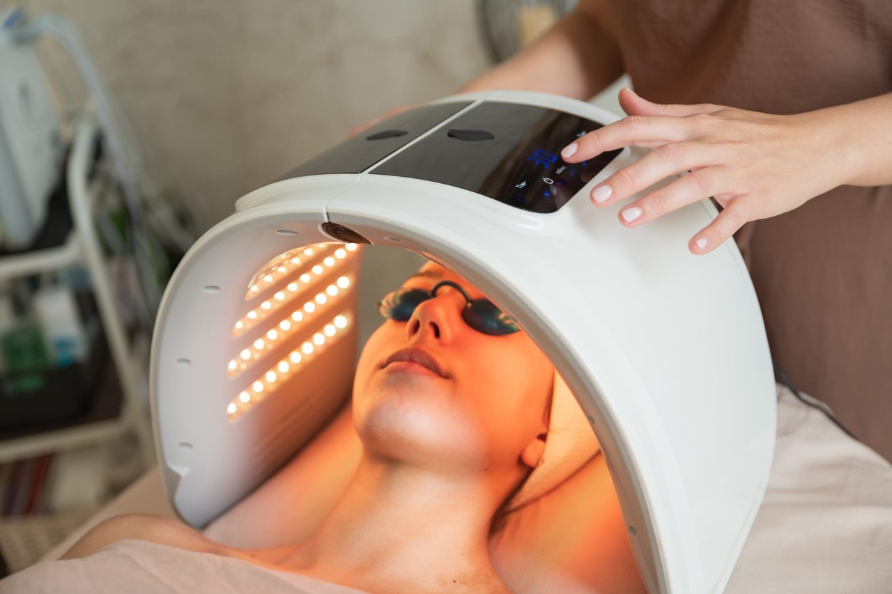 A client lying under an LED light therapy dome, wearing protective goggles.